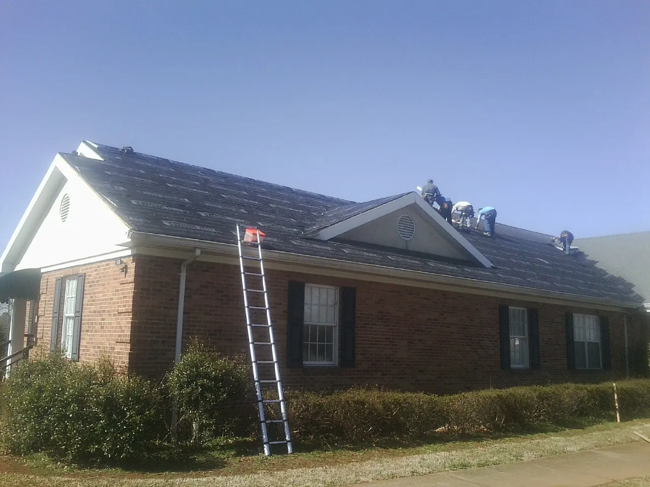 Crew tearing shingles off a brick ranch roof with a ladder set — Emergency Roof Repair work by our crew in Little York