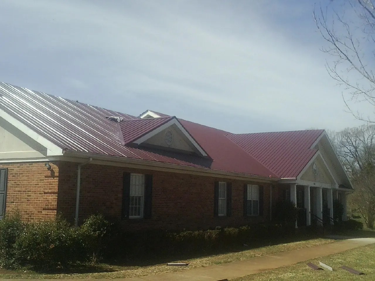 Red metal roof with gabled entries on a long brick building, from a Hail Damage Roof Repair job in Little York